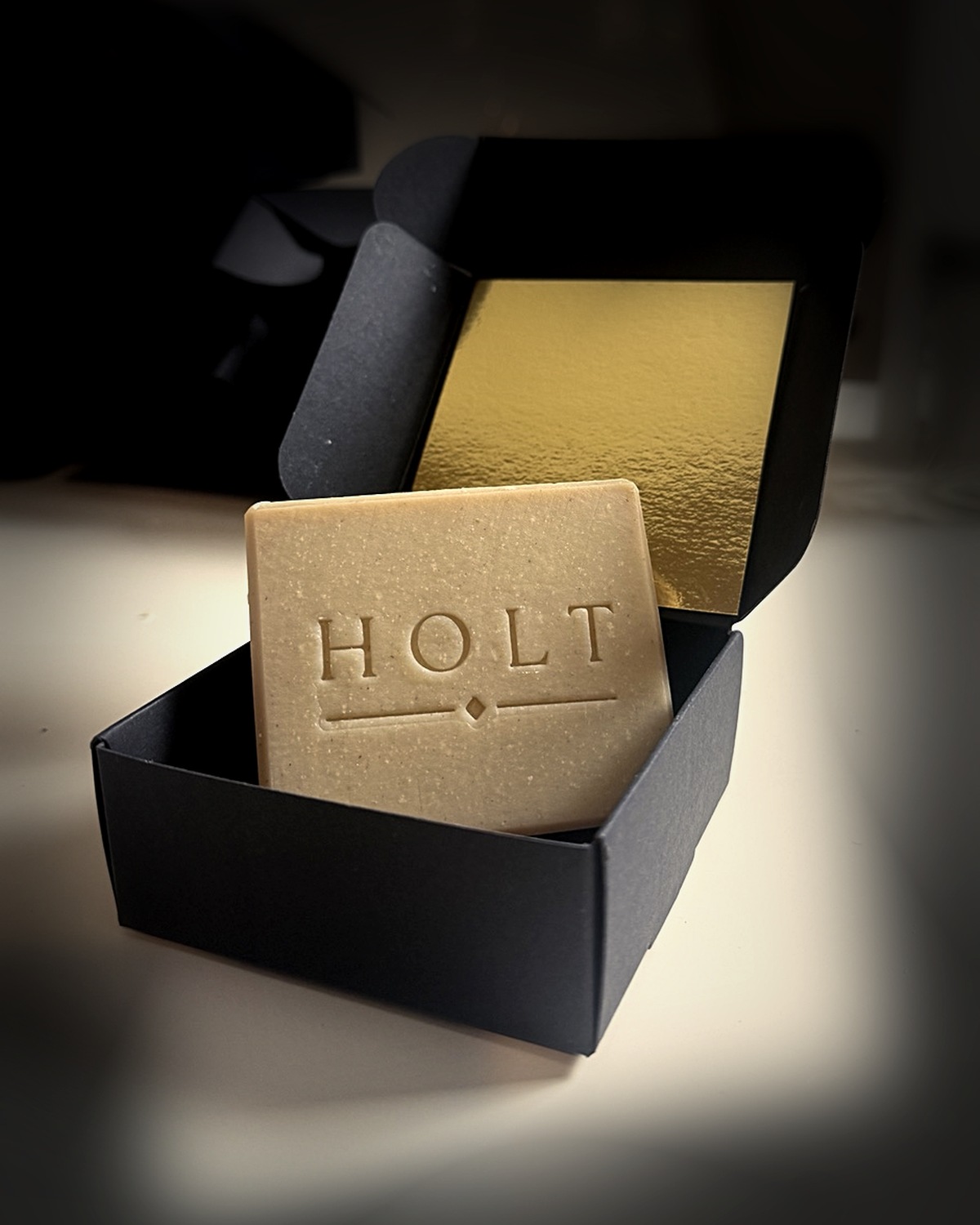 Embossed Holt soap bar displayed in a black box with a gold interior